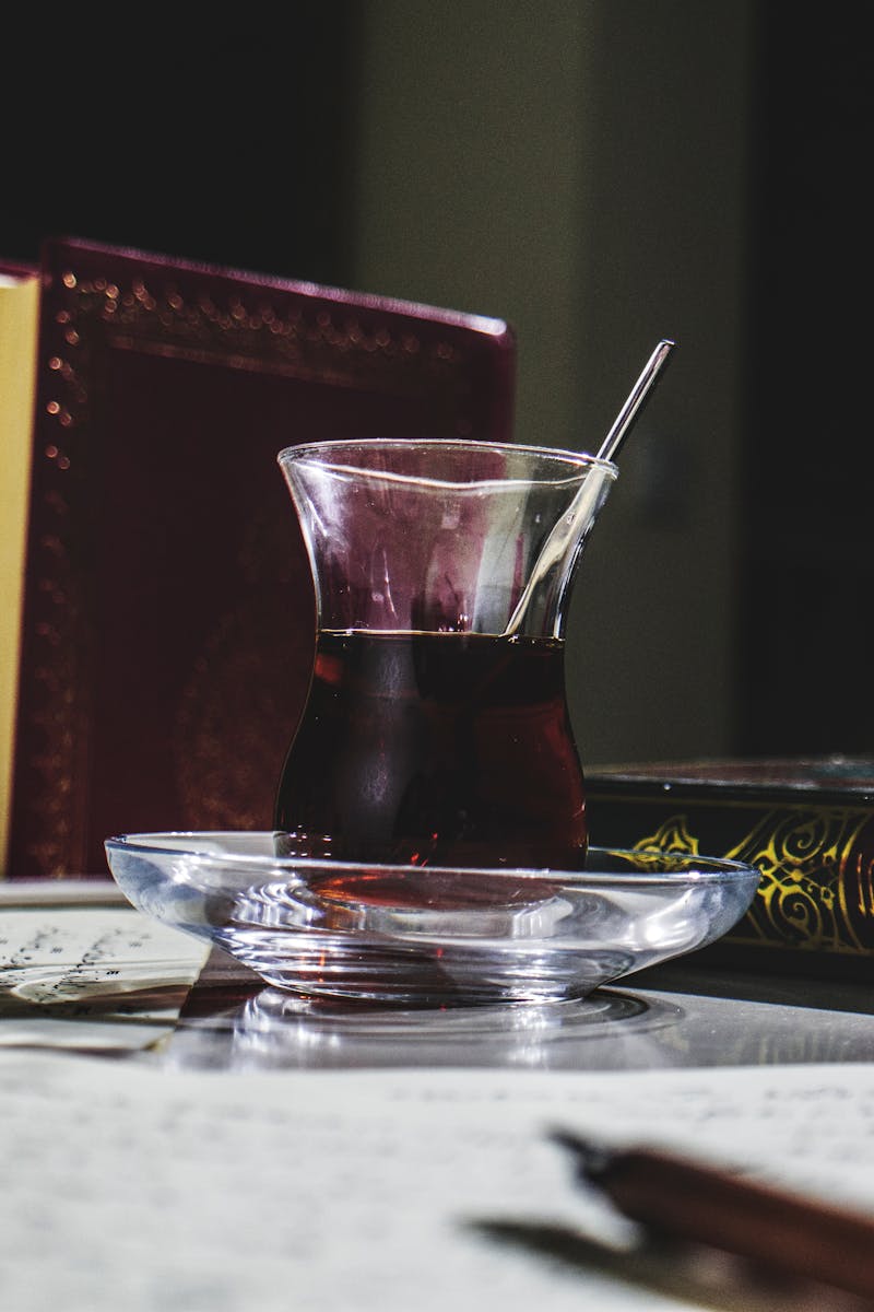 A glass of black tea on a table with ornate books including the Quran, enhancing a scholarly atmosphere.